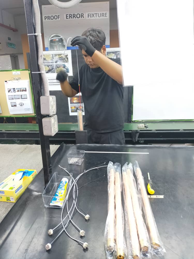 A technician inspecting brass lighting components during the quality control process at the Amat Sinar Lighting factory.