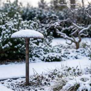 Close-up of a brass path light in a snowy landscape, showcasing its durable construction and elegant design, ideal for OEM landscape lighting projects.
