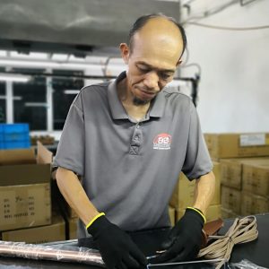 A factory worker assembling wiring components of a brass landscape light, showcasing precision and attention to detail.