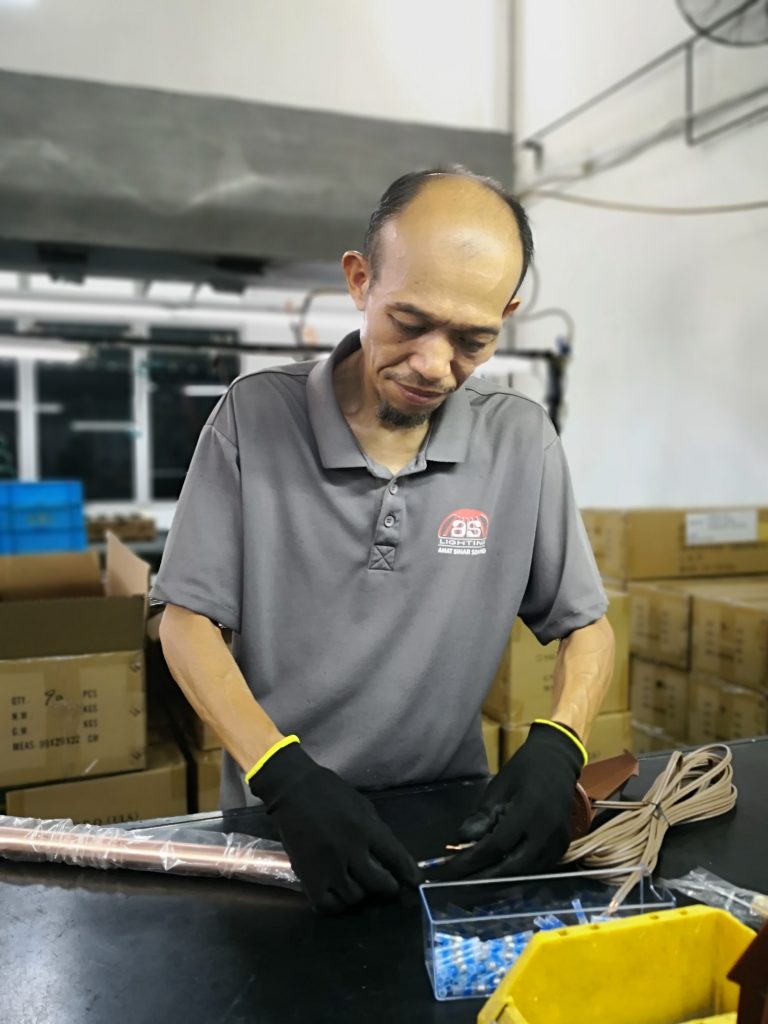 A factory worker assembling wiring components of a brass landscape light, showcasing precision and attention to detail.