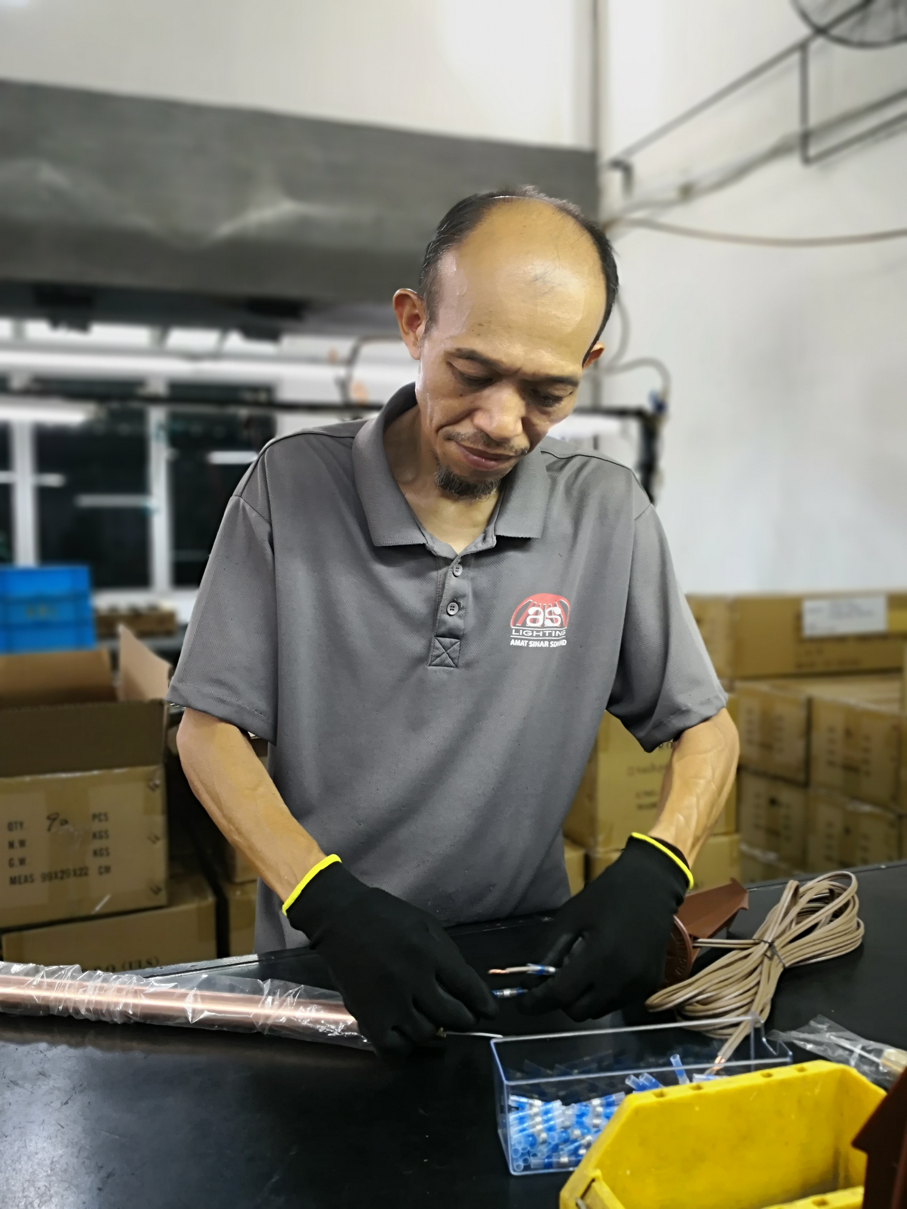 A factory worker assembling electrical components for brass landscape lighting, showcasing the precision and care taken in the manufacturing process.