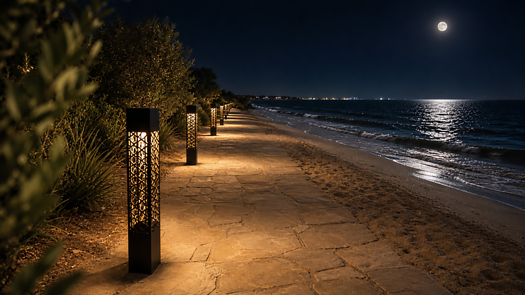 Black geometric bollard lights illuminating a stone pathway along a sandy beach at night, with the ocean and moon visible in the background.