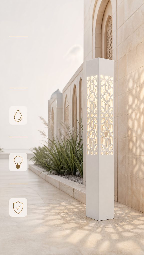 A modern white geometric bollard light with a laser-cut Arabic pattern, illuminating a pathway next to a light stone building and lush green plants.